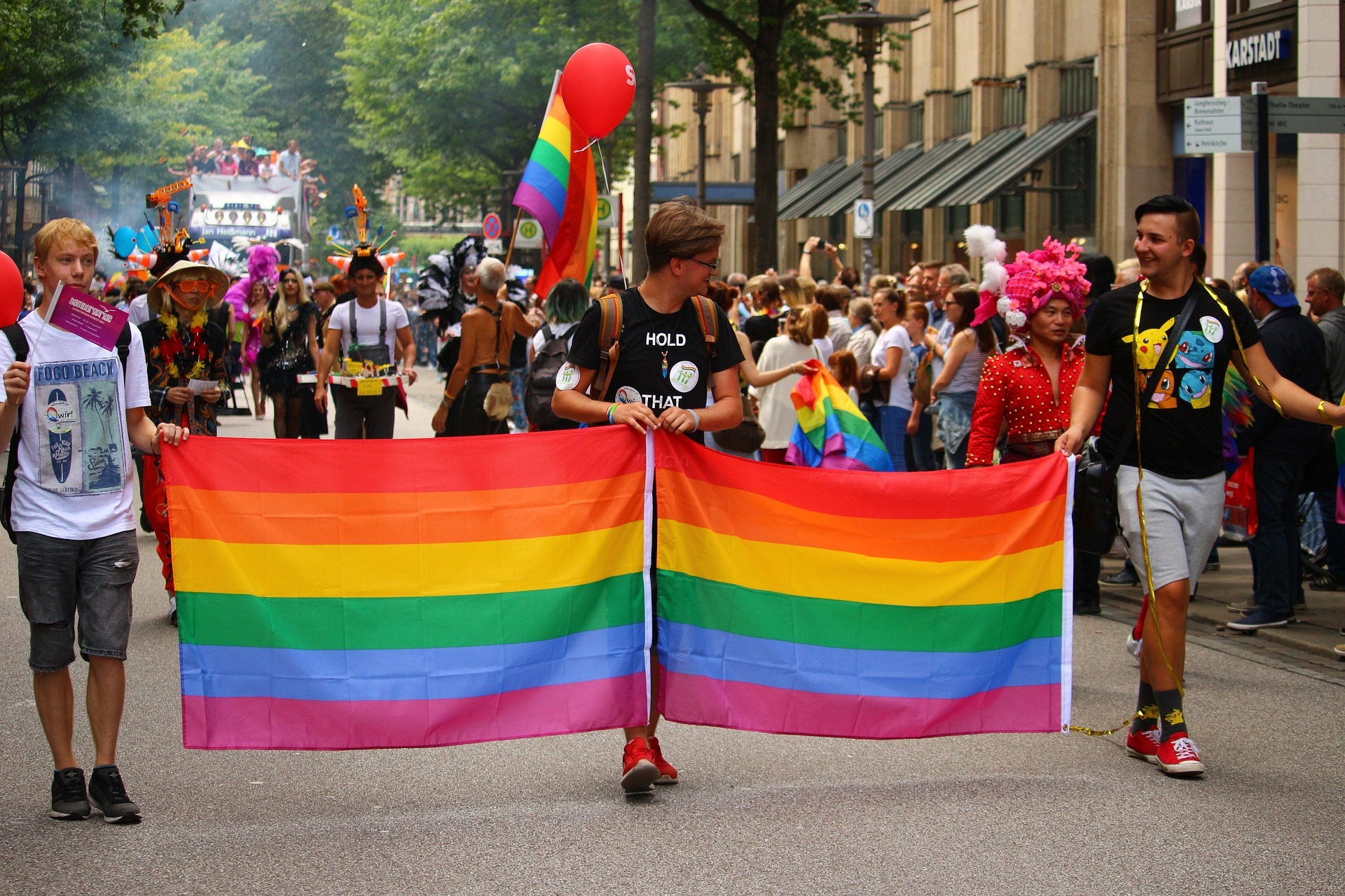 Three Men holding a rainbow flag followed by a group of people during a Pride parade.