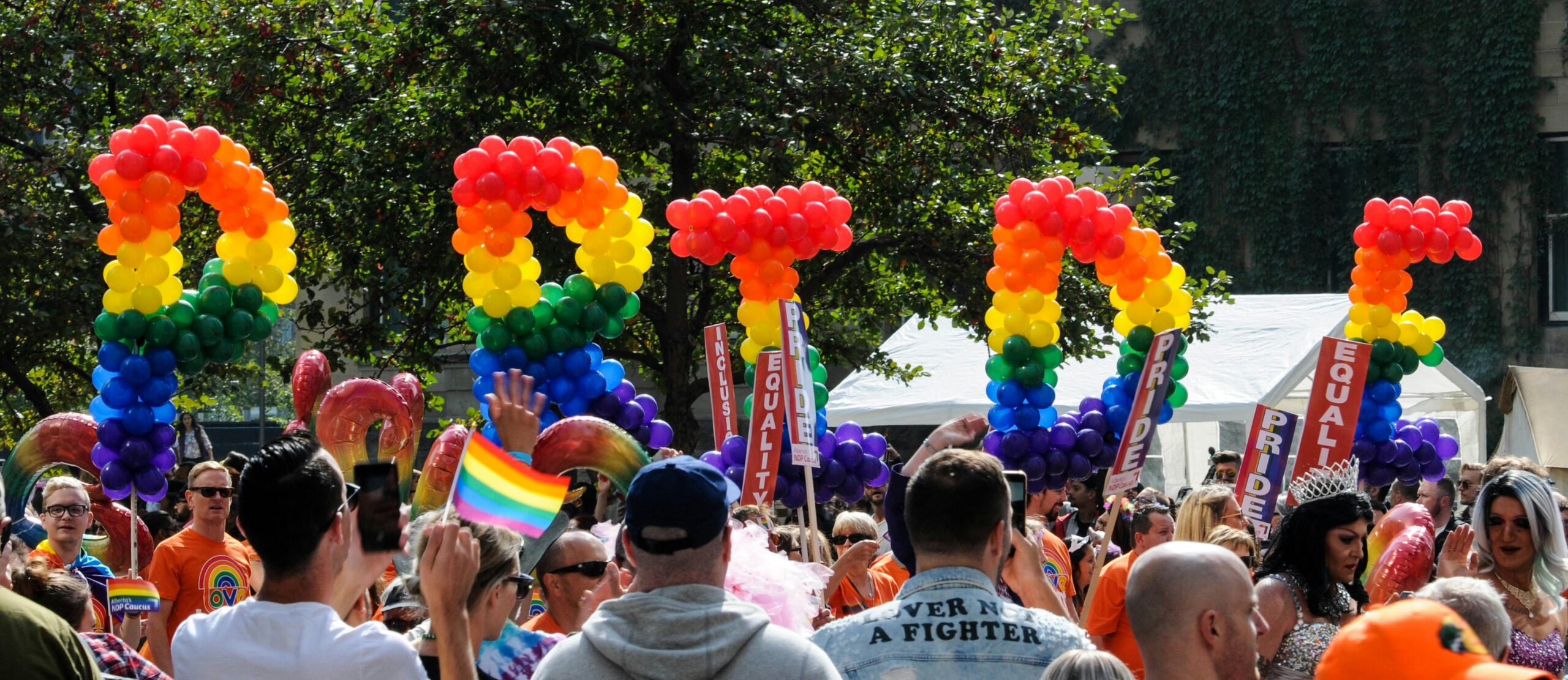 A group of people walking holding rainbow flags and the word "PRIDE" during a Pride parade.