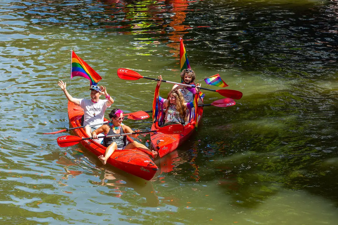 People in a river boat holding rainbow flags during Amsterdam Pride.