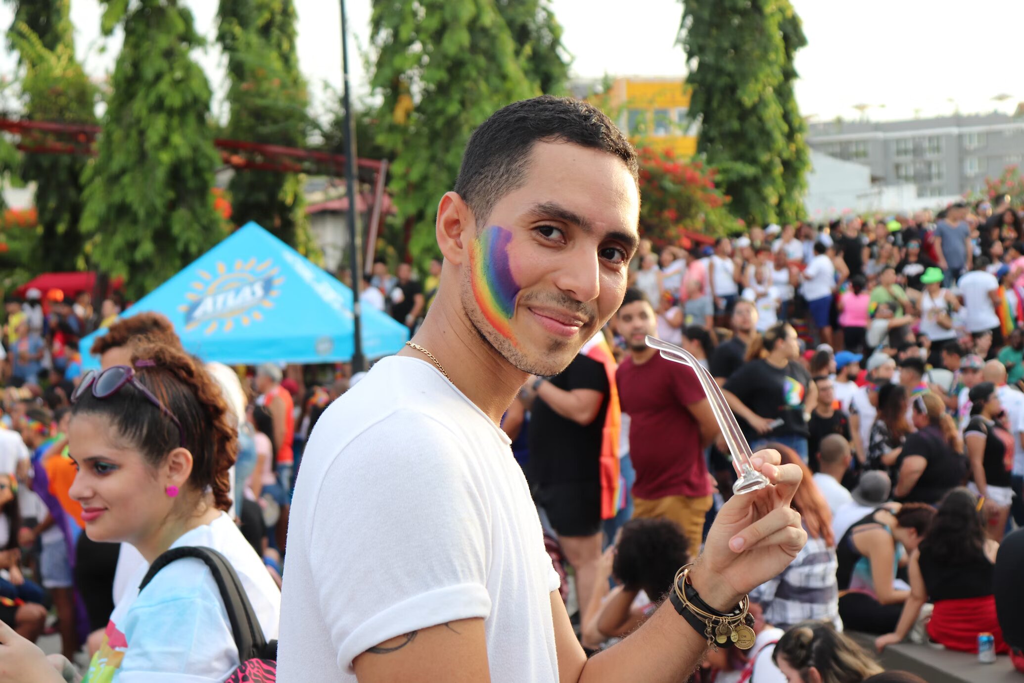 A guy smiling in a Pride parade surrounded by a group of people holding rainbow flags.